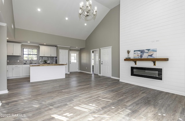 unfurnished living room with dark hardwood / wood-style flooring, a fireplace, high vaulted ceiling, and a chandelier