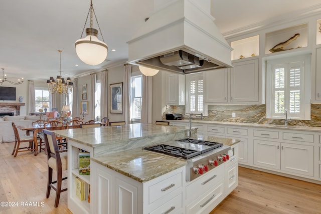 kitchen with custom exhaust hood, stainless steel gas cooktop, a center island, light hardwood / wood-style floors, and hanging light fixtures