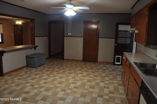 kitchen with a wainscoted wall, light countertops, ceiling fan, a sink, and dishwashing machine