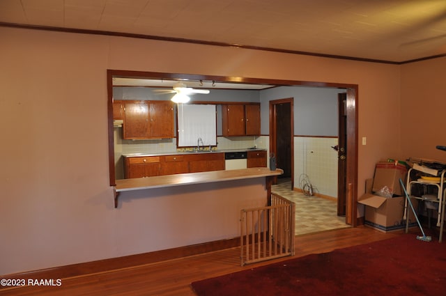 kitchen with kitchen peninsula, ornamental molding, sink, wood-type flooring, and dishwasher