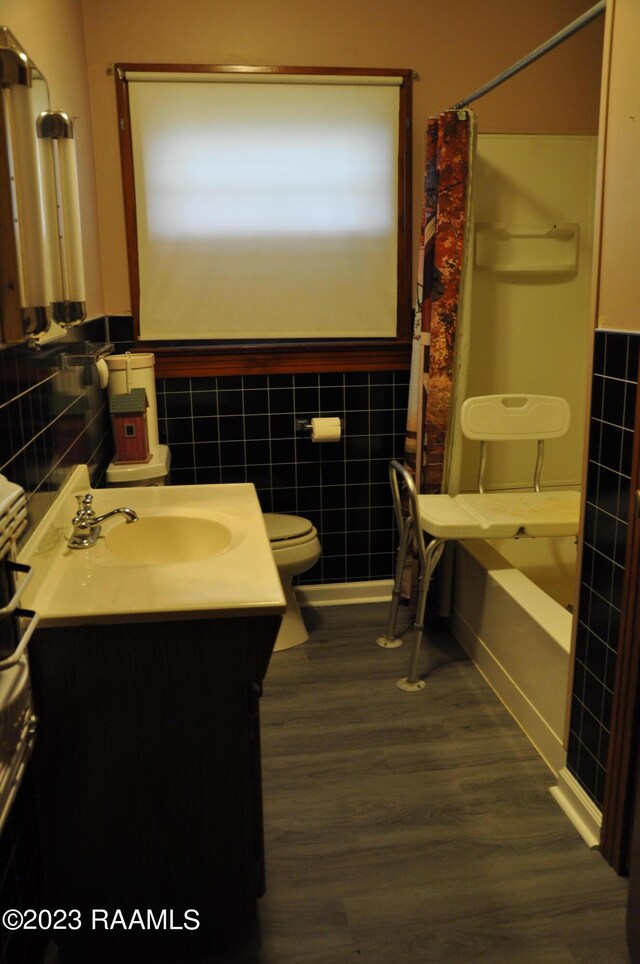 full bathroom featuring hardwood / wood-style floors, toilet, shower / bath combo with shower curtain, vanity, and tile walls