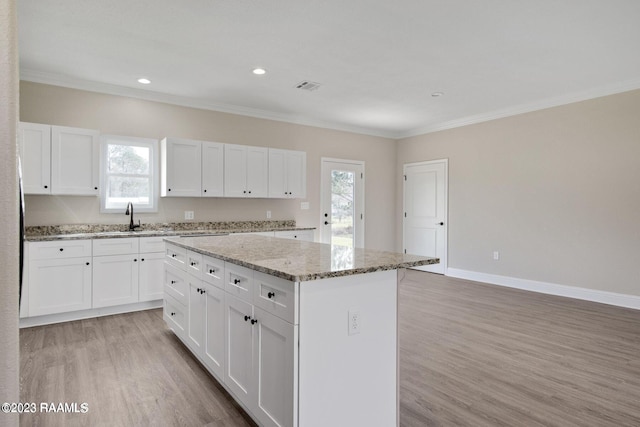 kitchen featuring light wood-style flooring, visible vents, baseboards, ornamental molding, and a center island