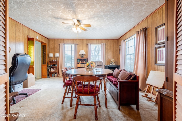 carpeted dining space with wood walls, ceiling fan, and a textured ceiling