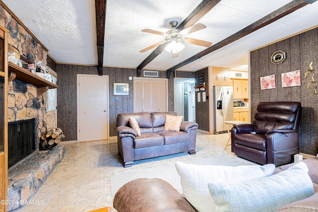 tiled living room featuring ceiling fan, a stone fireplace, beam ceiling, and a textured ceiling