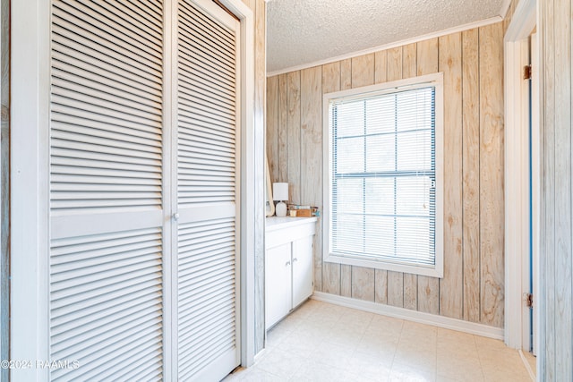 hall with wood walls, crown molding, light tile floors, and a textured ceiling