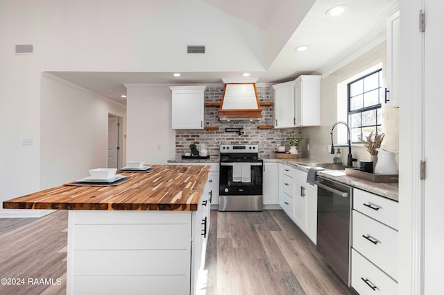 kitchen featuring a center island, stainless steel appliances, premium range hood, white cabinetry, and light hardwood / wood-style flooring