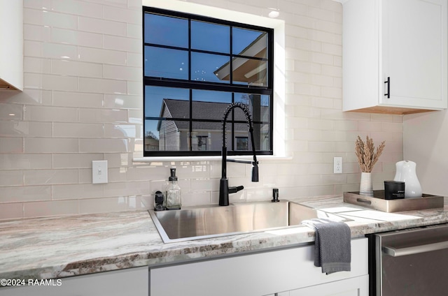 kitchen featuring white cabinets, backsplash, stainless steel dishwasher, and light stone counters