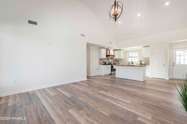 unfurnished living room with high vaulted ceiling, light hardwood / wood-style floors, an inviting chandelier, and sink