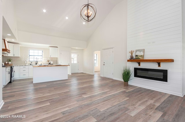 unfurnished living room with high vaulted ceiling, an inviting chandelier, and hardwood / wood-style floors