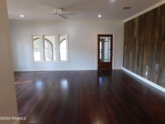 spare room with crown molding, dark hardwood / wood-style flooring, wooden walls, and ceiling fan