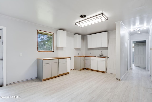 kitchen featuring light wood-type flooring, sink, ornamental molding, and white cabinets