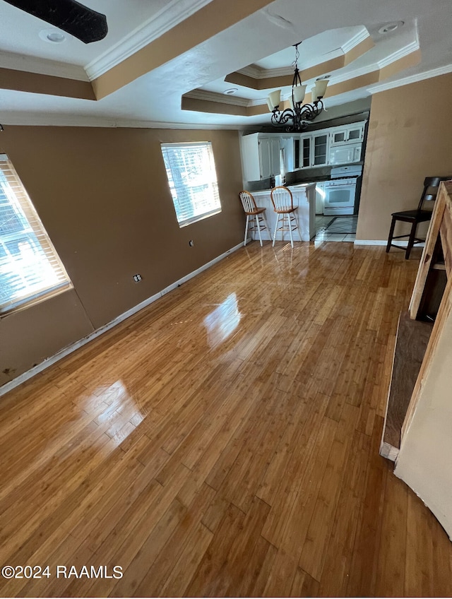 empty room featuring a chandelier, wood-type flooring, a tray ceiling, and ornamental molding