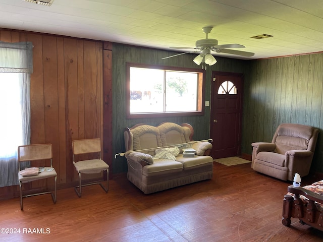 living room with wood-type flooring, wood walls, and ceiling fan