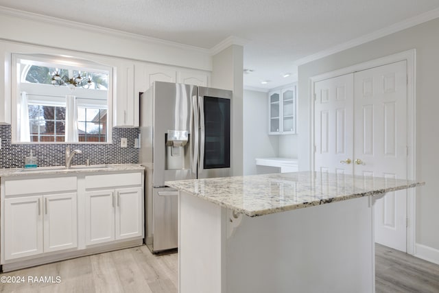 kitchen with stainless steel fridge with ice dispenser, light hardwood / wood-style floors, a kitchen island, and tasteful backsplash