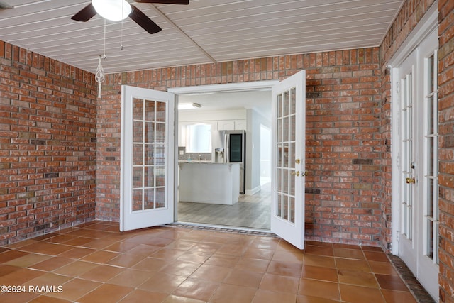 spare room featuring brick wall, tile flooring, ceiling fan, and french doors