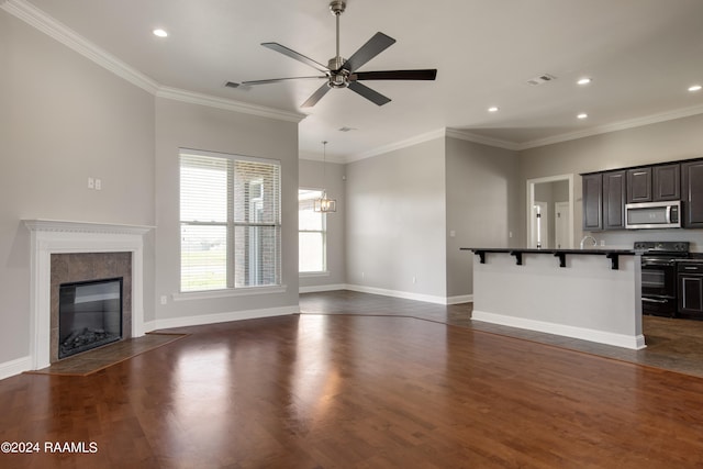 unfurnished living room with crown molding, a tile fireplace, dark wood-type flooring, and ceiling fan with notable chandelier