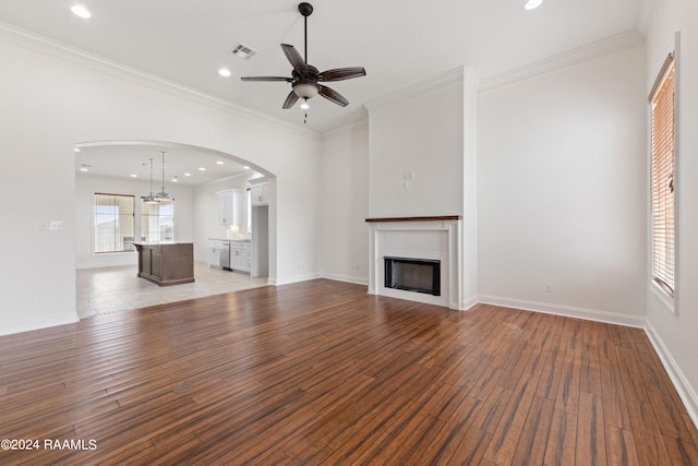 unfurnished living room featuring a tiled fireplace, ceiling fan, dark wood-type flooring, and ornamental molding