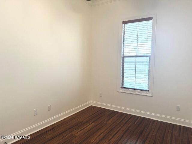 empty room with dark hardwood / wood-style floors and crown molding