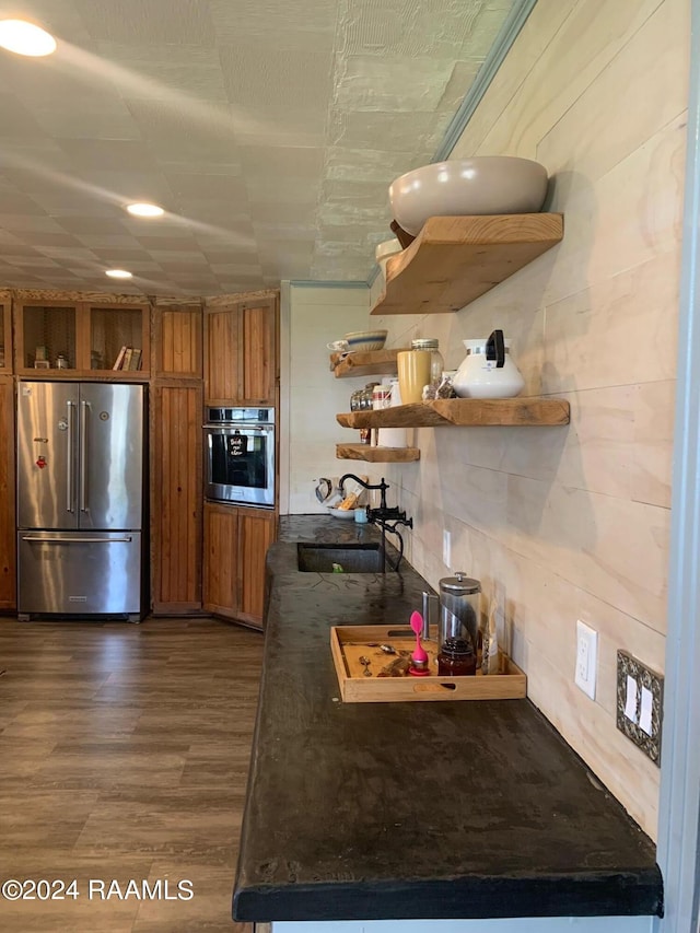 kitchen featuring dark wood-type flooring, appliances with stainless steel finishes, dark stone countertops, and sink
