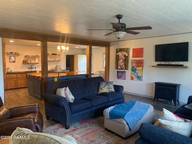 living room featuring a textured ceiling, a wood stove, wood-type flooring, and ceiling fan with notable chandelier