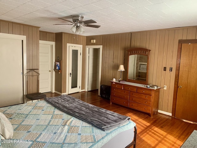 bedroom featuring wooden walls, ceiling fan, and dark wood-type flooring