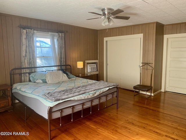 bedroom featuring wood walls, wood-type flooring, ceiling fan, and a wall unit AC