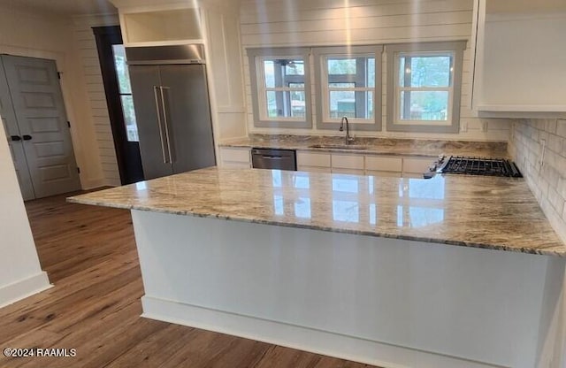 kitchen with white cabinets, appliances with stainless steel finishes, light stone counters, sink, and dark wood-type flooring