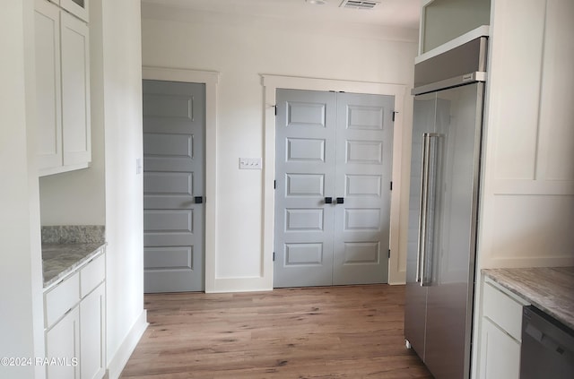 kitchen with built in fridge, black dishwasher, white cabinetry, and light hardwood / wood-style flooring