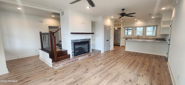 unfurnished living room with built in shelves, ceiling fan, ornamental molding, and light wood-type flooring