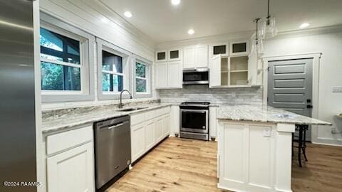 kitchen featuring light wood-type flooring, appliances with stainless steel finishes, white cabinetry, and light stone counters