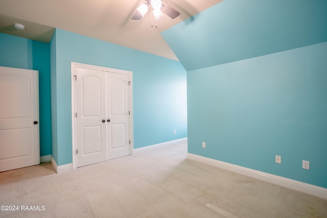 unfurnished bedroom featuring ceiling fan, a closet, light colored carpet, and vaulted ceiling