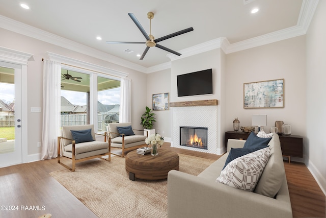 living room featuring ceiling fan, ornamental molding, a fireplace, and light wood-type flooring