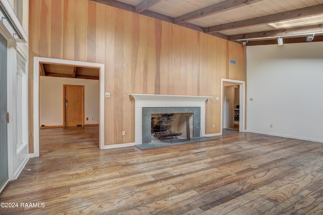 unfurnished living room with beam ceiling, wood ceiling, light wood-type flooring, and wooden walls