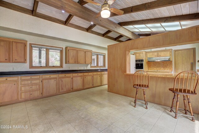 kitchen with ceiling fan, a kitchen bar, light tile floors, stainless steel oven, and lofted ceiling with beams