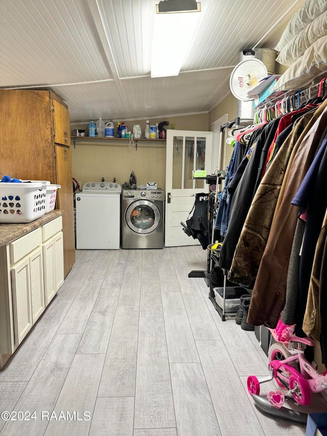 clothes washing area featuring washing machine and dryer, light hardwood / wood-style flooring, and cabinets