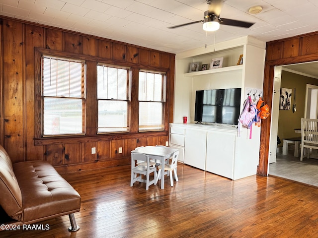 living area with ceiling fan, wood walls, and hardwood / wood-style flooring