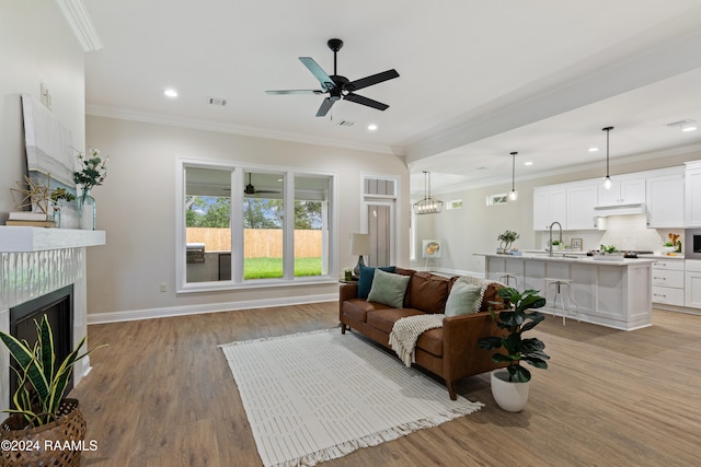 living room featuring ceiling fan, sink, a premium fireplace, light hardwood / wood-style flooring, and ornamental molding