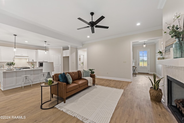 living room with ceiling fan, ornamental molding, a tiled fireplace, and light wood-type flooring