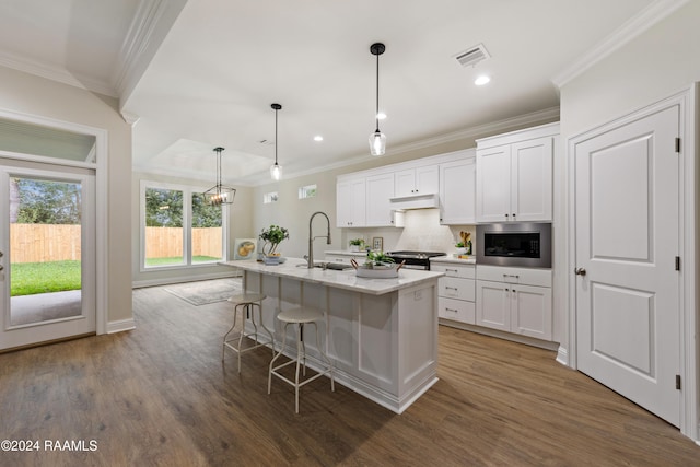 kitchen with white cabinetry, pendant lighting, built in microwave, and a kitchen island with sink