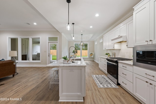 kitchen with gas stove, white cabinetry, an island with sink, hanging light fixtures, and light wood-type flooring