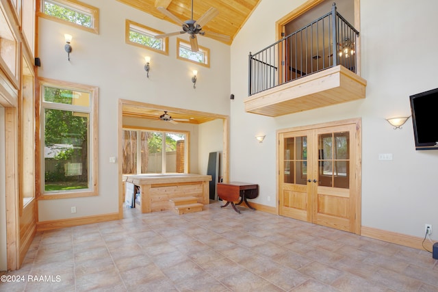 unfurnished living room featuring french doors, light tile floors, ceiling fan, and a high ceiling