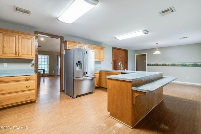 kitchen with hanging light fixtures, a breakfast bar area, stainless steel refrigerator with ice dispenser, and light hardwood / wood-style flooring