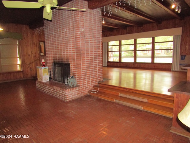 unfurnished living room with ceiling fan, beamed ceiling, a brick fireplace, wood-type flooring, and brick wall