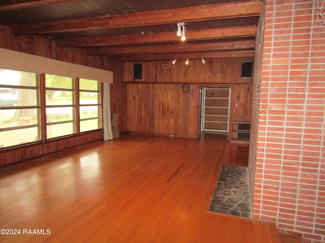 unfurnished living room with hardwood / wood-style floors, wooden walls, and beam ceiling