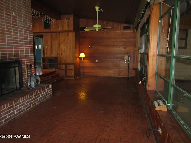 interior space with ceiling fan, vaulted ceiling, wood walls, and a brick fireplace