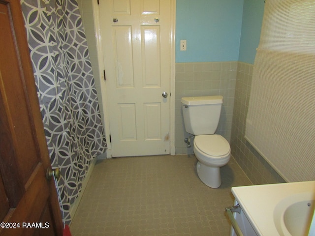 bathroom featuring tile flooring, vanity, toilet, and tile walls