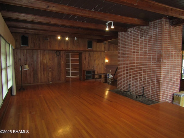unfurnished living room featuring beamed ceiling, wooden walls, and wood finished floors