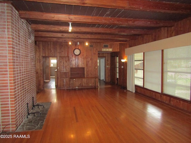 unfurnished living room featuring wooden walls, wood finished floors, and beamed ceiling
