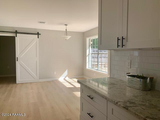 kitchen featuring light wood finished floors, a barn door, baseboards, light stone countertops, and white cabinetry