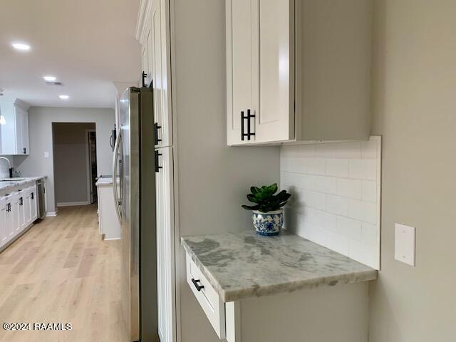 kitchen featuring light stone counters, stainless steel appliances, white cabinets, a sink, and light wood-type flooring